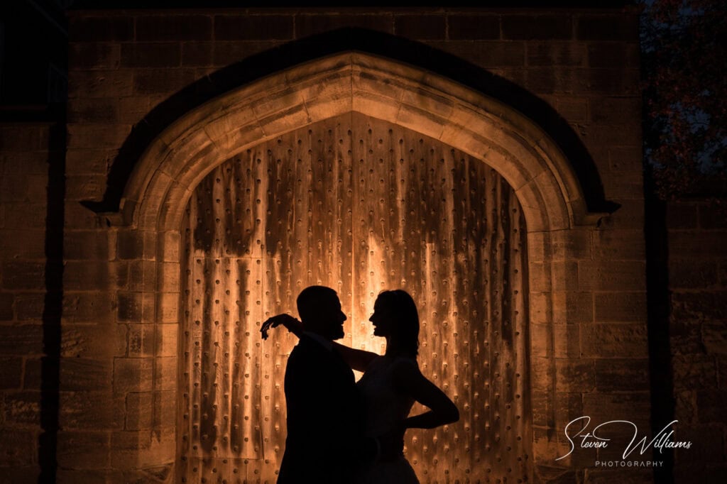 Silhouetted couple dancing, historic door backdrop, night photography.