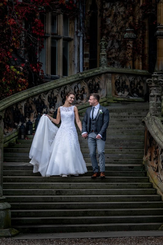 Bride and groom descending historic mansion staircase.