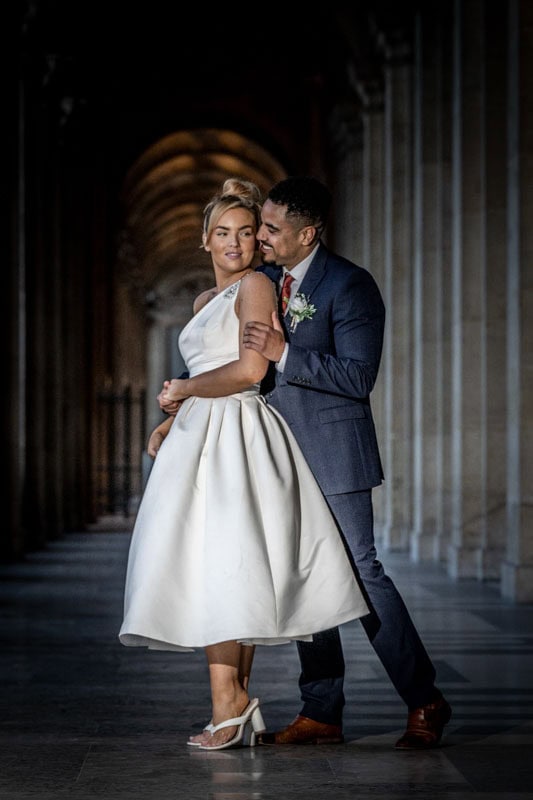 Couple in wedding attire embracing in corridor.