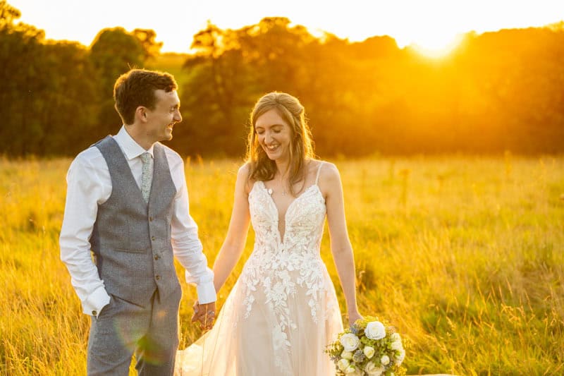 Couple in wedding attire enjoying sunset in a field.