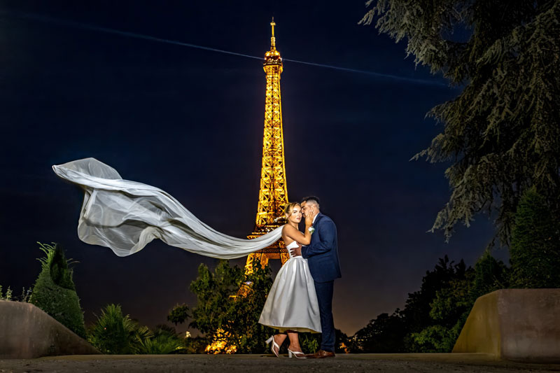 Couple kissing by Eiffel Tower at night, veil floating.