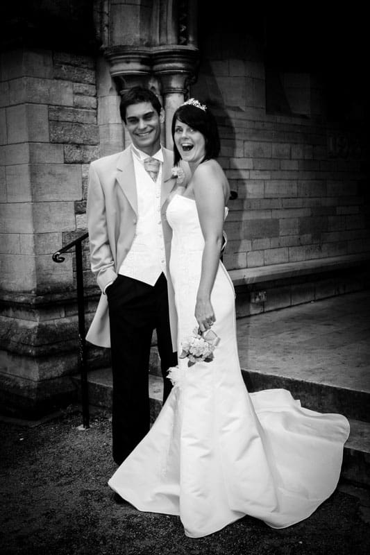 Joyful newlyweds posing outside traditional wedding venue.