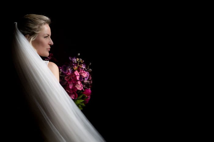 Bride with veil holding vibrant bouquet, dark background.