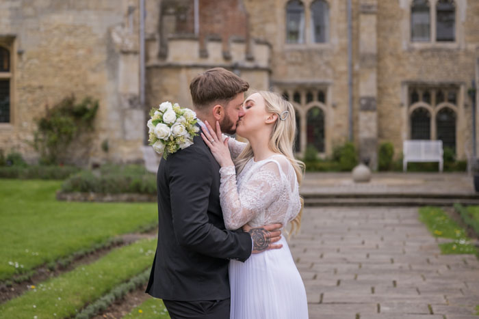Couple kissing outside historic building on wedding day.